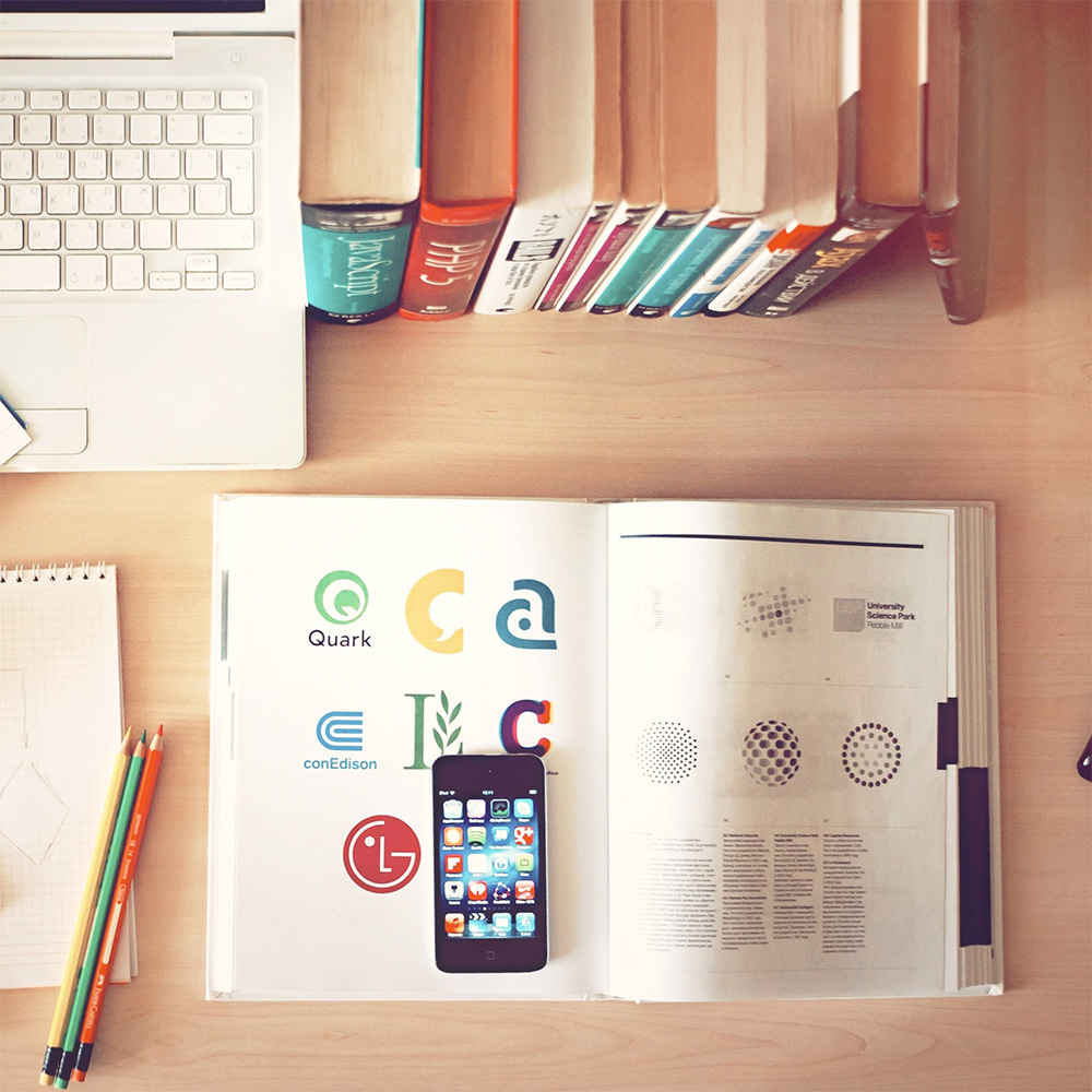 Arbeitsplatz – Laptop, Skizzen, Buch mit Logo Designs